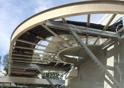 Damaged curved roof structure with exposed beams and debris at a building site