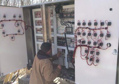 Technician inspecting electrical panels with wiring and meters outdoors in a snowy area