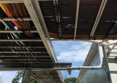 Underside of a pedestrian walkway with metal beams and stairs against a blue sky.