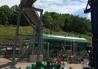 Industrial facility with green tanks and metal scaffolding outdoors, surrounded by trees