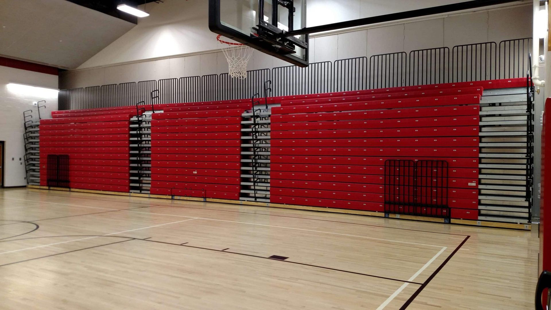Red folding gym bleachers stacked against a wall in an empty indoor basketball court.
