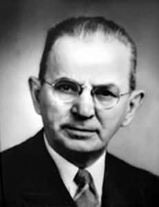 Black-and-white portrait of a man in glasses and a suit, facing the camera with a serious expression