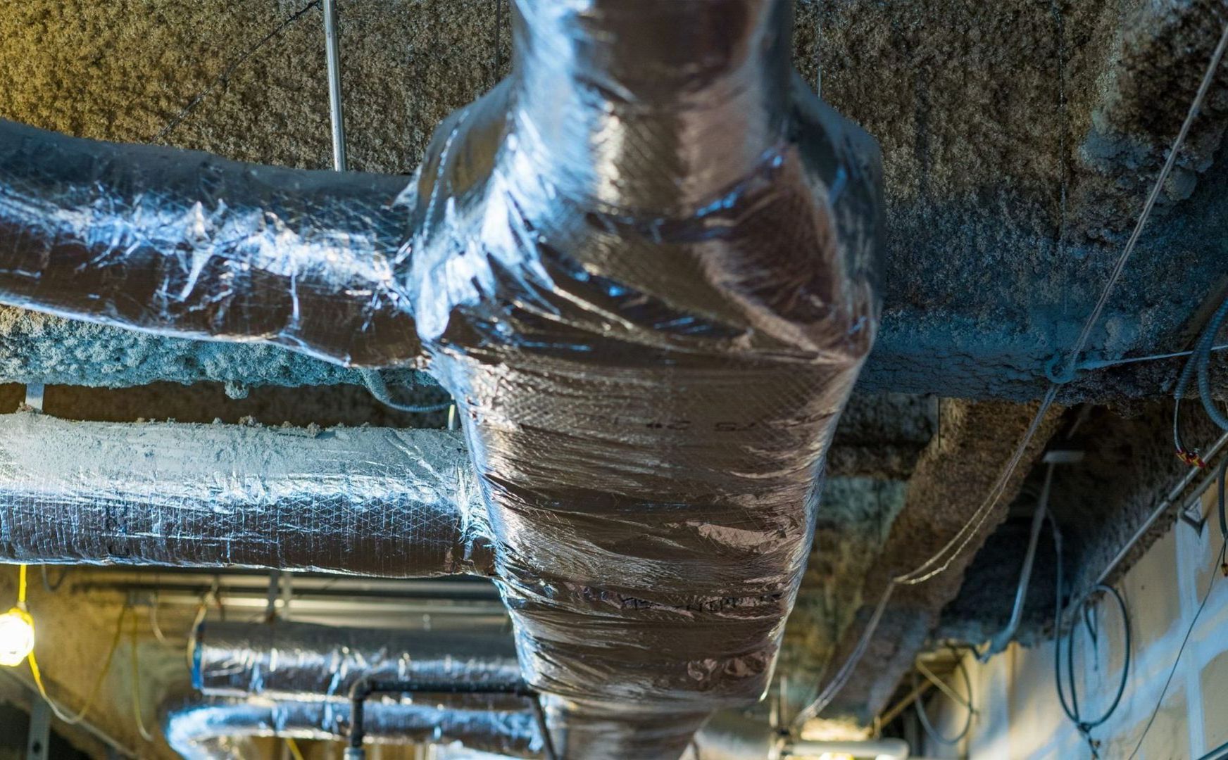 Insulated HVAC ducts and pipes running across a ceiling in an industrial space