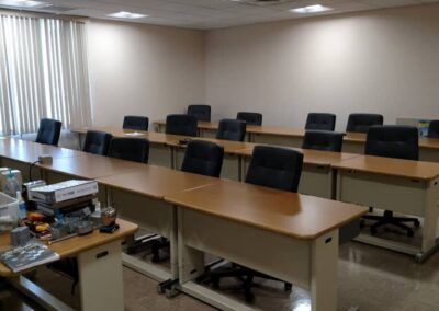 Empty conference room with long table, black chairs, and blinds on the left wall.