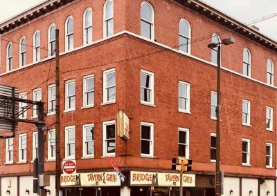 Red brick corner building with storefront signs and arched windows on a city street.