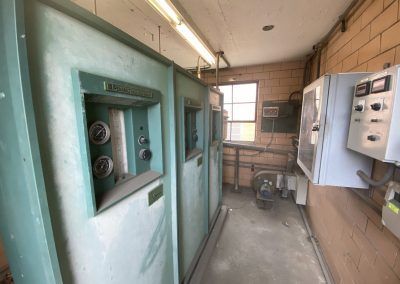 Industrial electrical room with teal control panels, meters, wiring, and a window at the back.