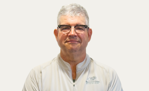 Man in glasses wearing a white collared shirt, standing against a light background, slight smile