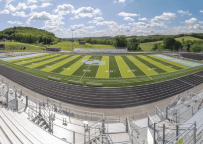 Empty football stadium with green turf, black track, and hills under a cloudy sky