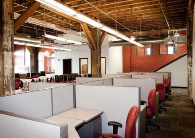 Open-plan office with gray cubicles, red chairs, and exposed wooden ceiling beams