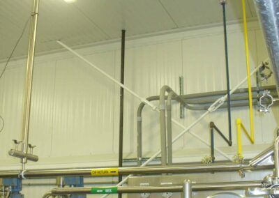 Industrial piping and hoses inside a utility room with metal equipment and yellow safety railings