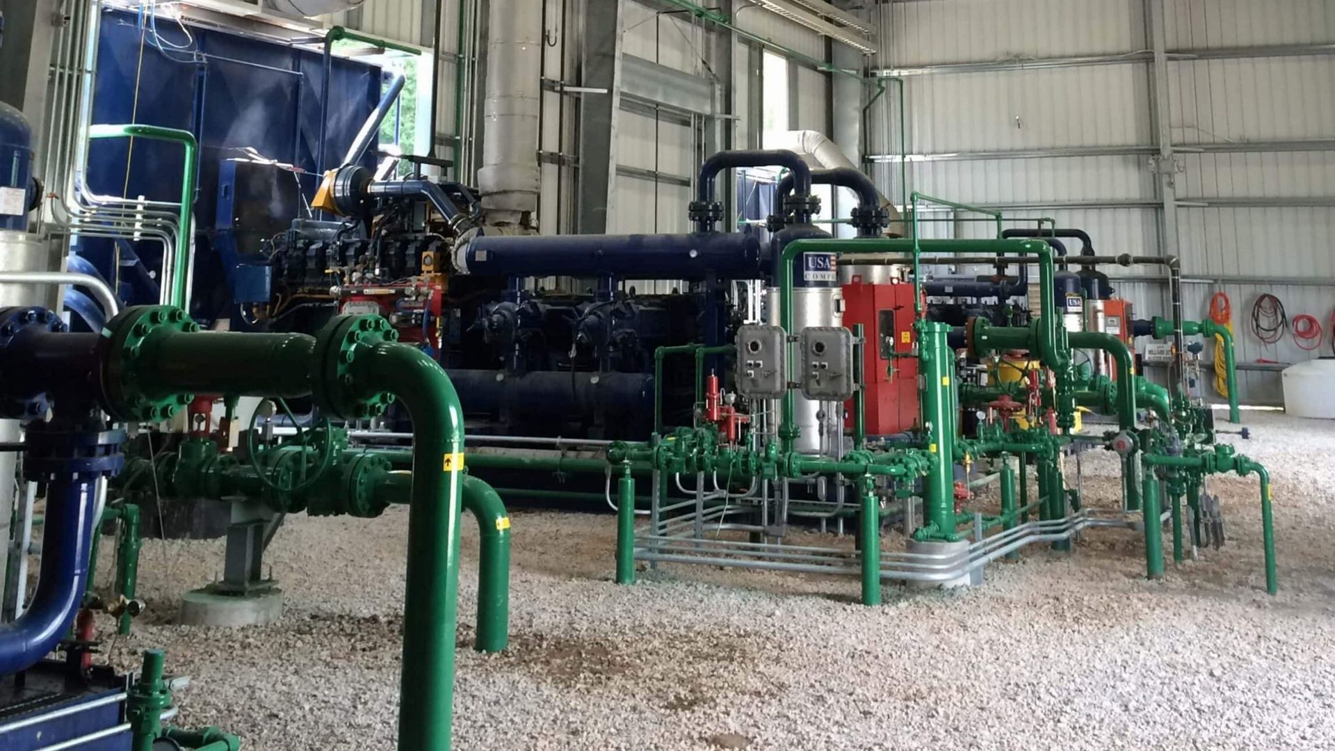 Industrial machinery in a factory, with green pipes, tanks, and metal equipment inside a large workshop.