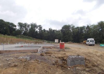 Construction site with concrete foundation, dirt lot, trees, and a white van in the background