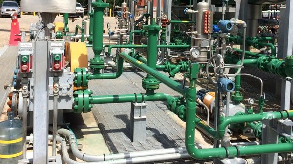 Industrial pipes and valves in a mechanical plant, with green and silver piping and gauges.