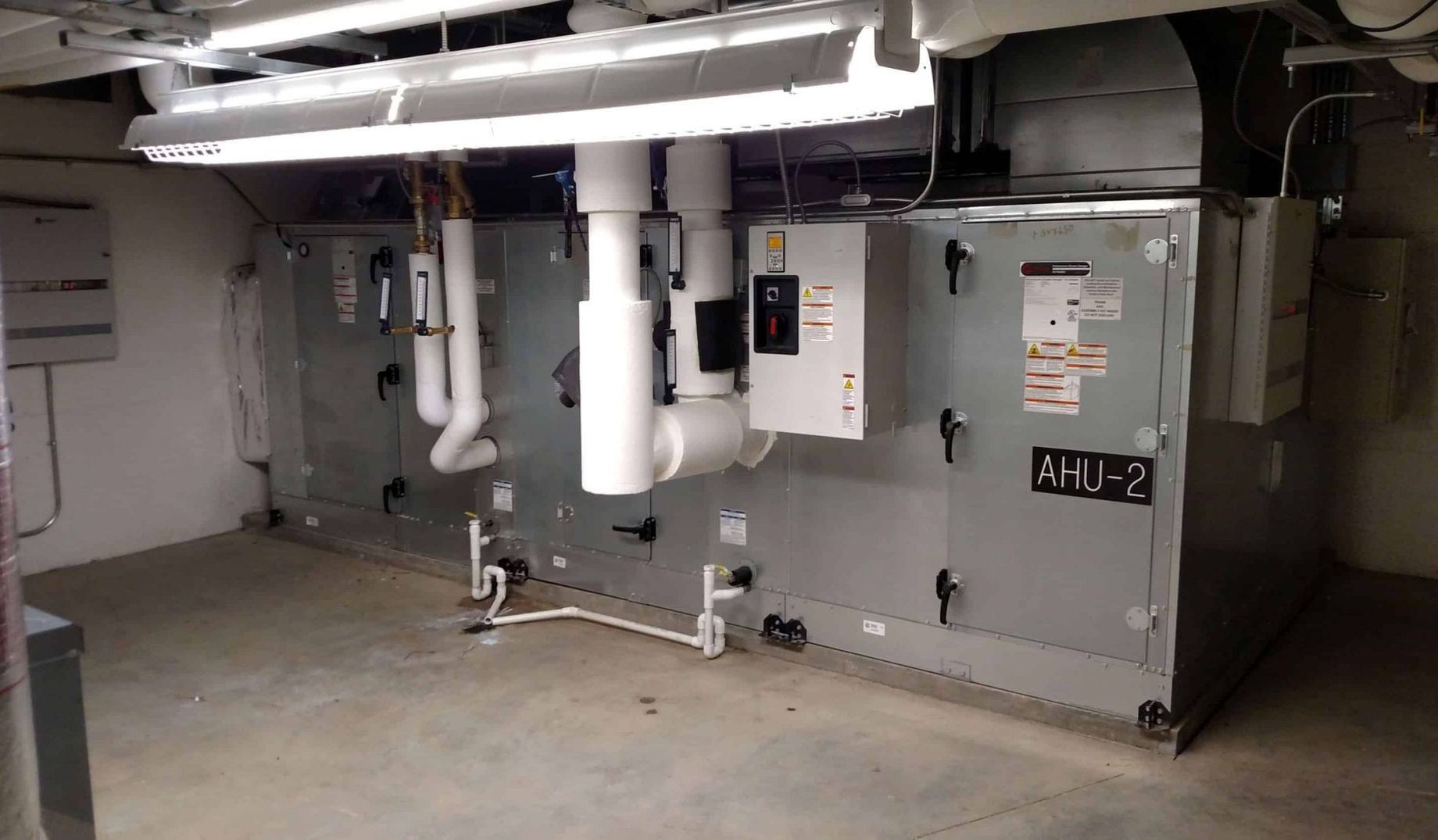 Basement utility room with large gray HVAC equipment, white pipes, and exposed ceiling ducts