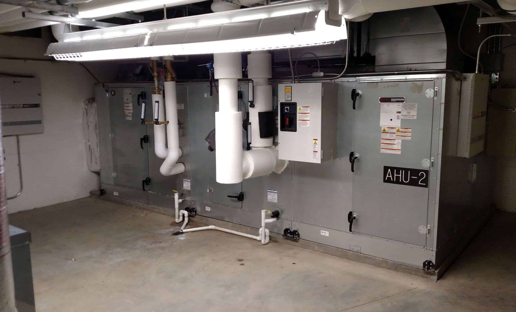 Basement utility room with HVAC equipment, white pipes, and a gray mechanical unit.