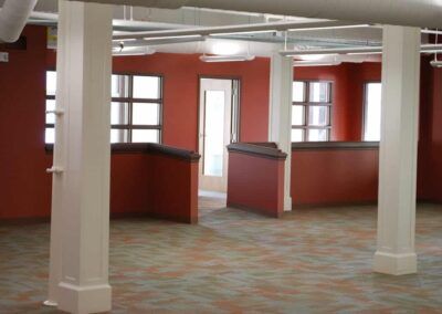 Empty red-walled room with white columns, windows, and carpeted floor