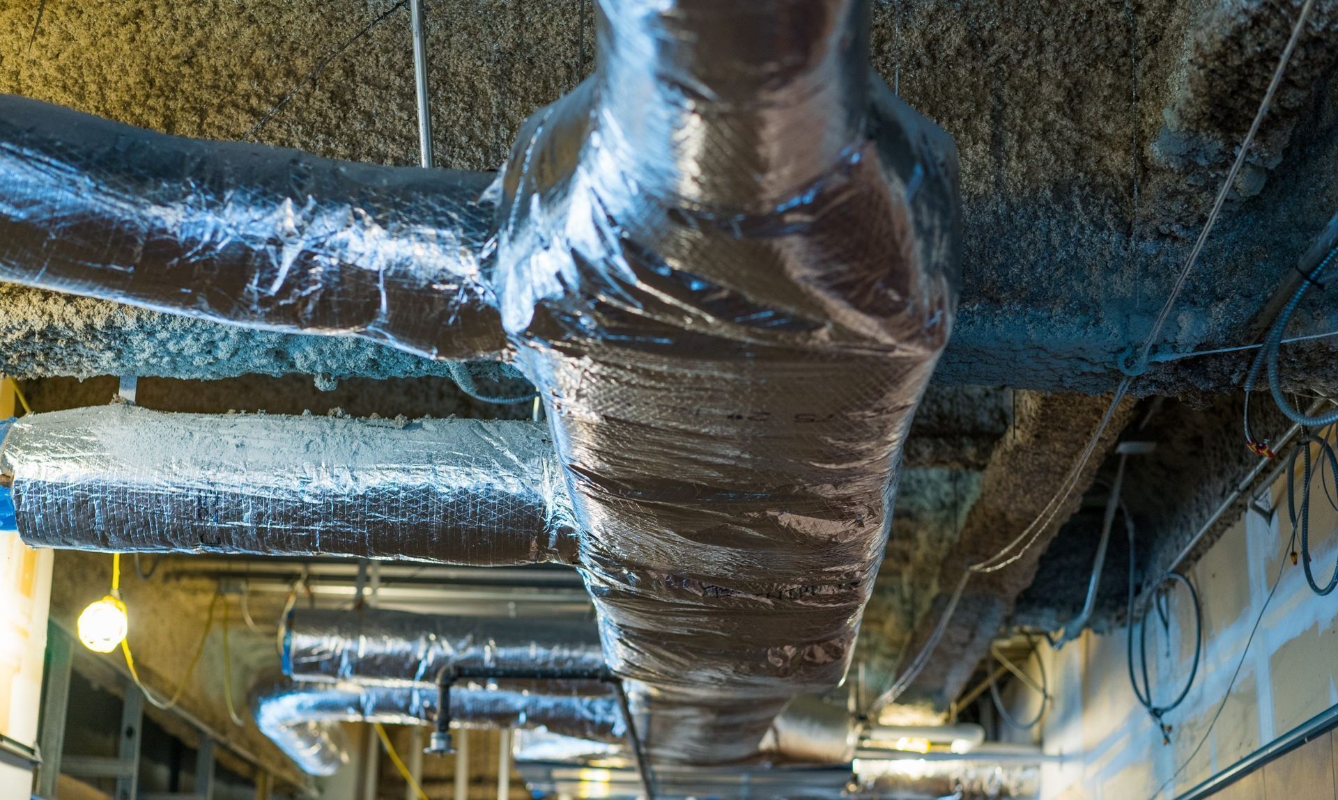 Insulated HVAC ductwork and pipes on a ceiling in an industrial utility space