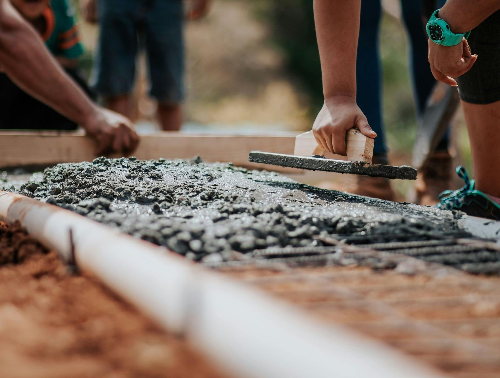 Hands smoothing wet concrete in a wooden form during sidewalk construction