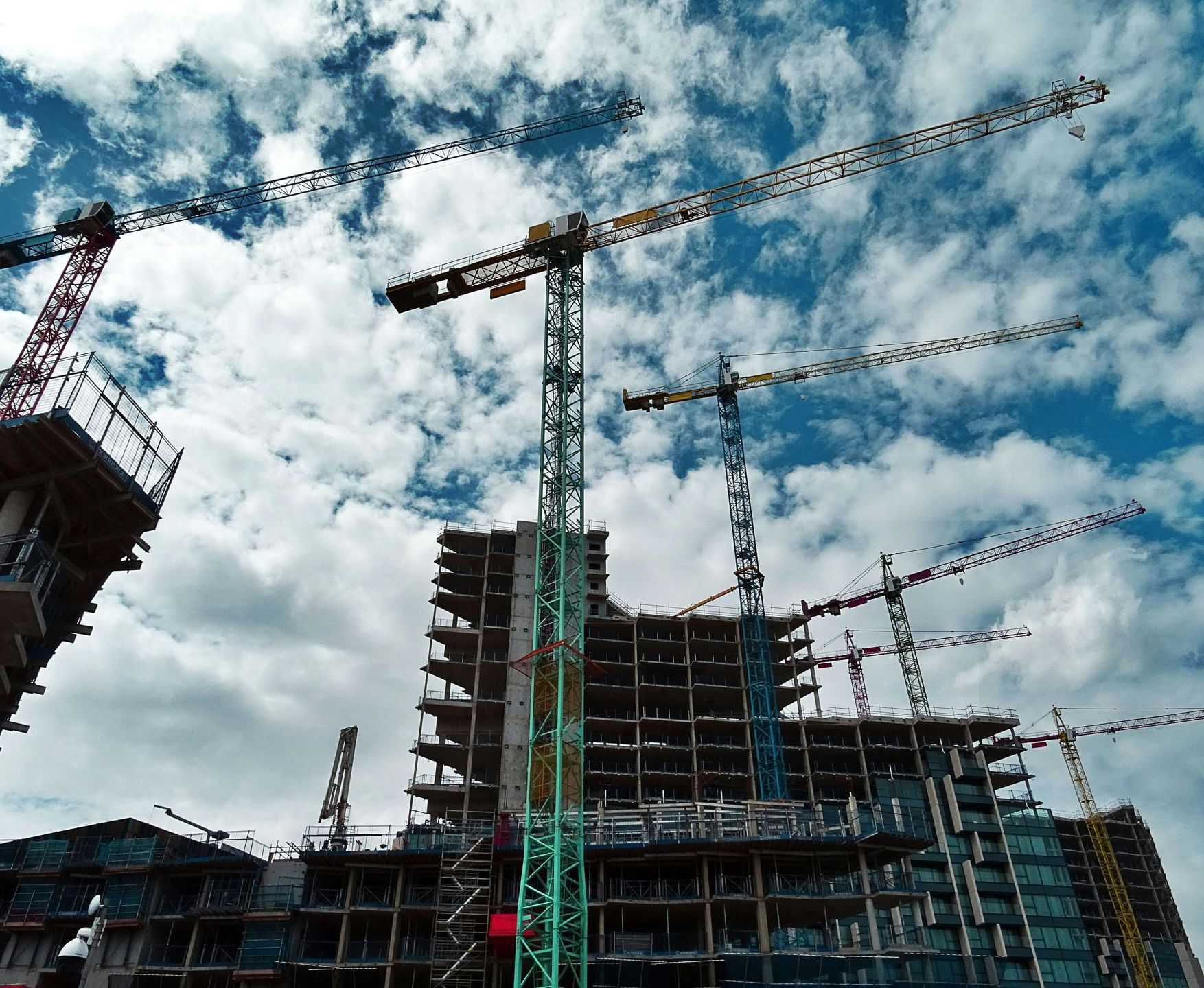 Construction site with tall cranes and unfinished buildings against a cloudy blue sky
