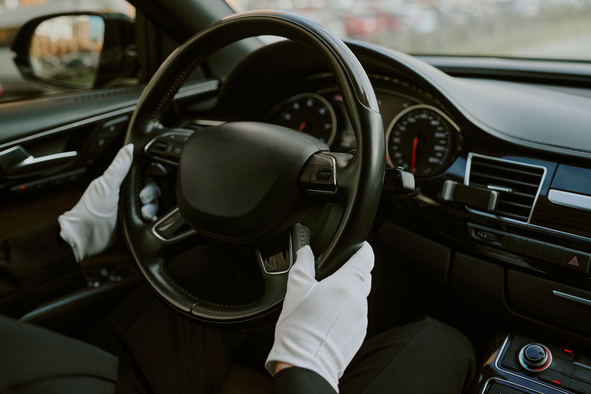 Hands in white gloves holding a black car steering wheel inside a luxury car interior