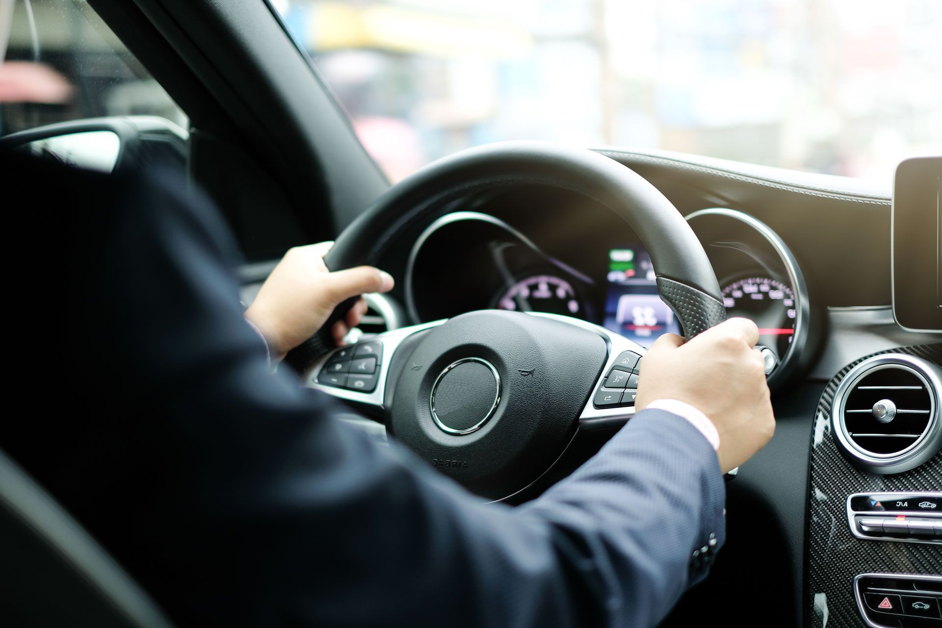 Driver holding a steering wheel inside a modern car, with dashboard and center console visible