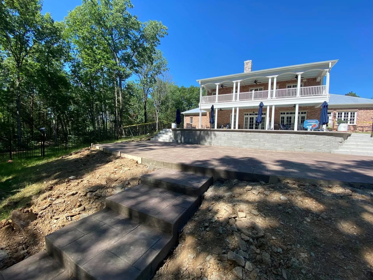 A large house with a patio and stairs in front of it is surrounded by trees.
