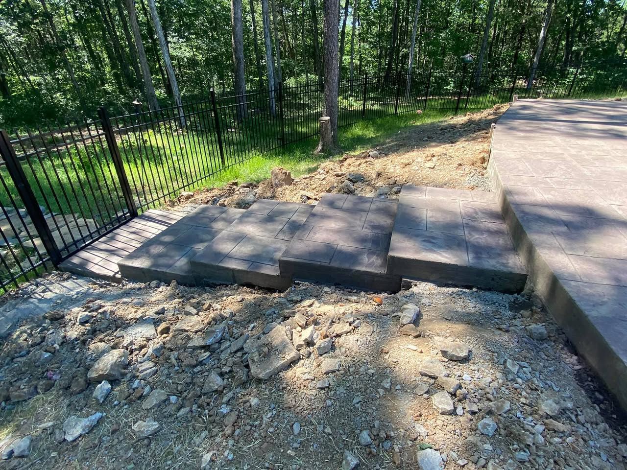 A concrete walkway is being built in the dirt next to a fence.