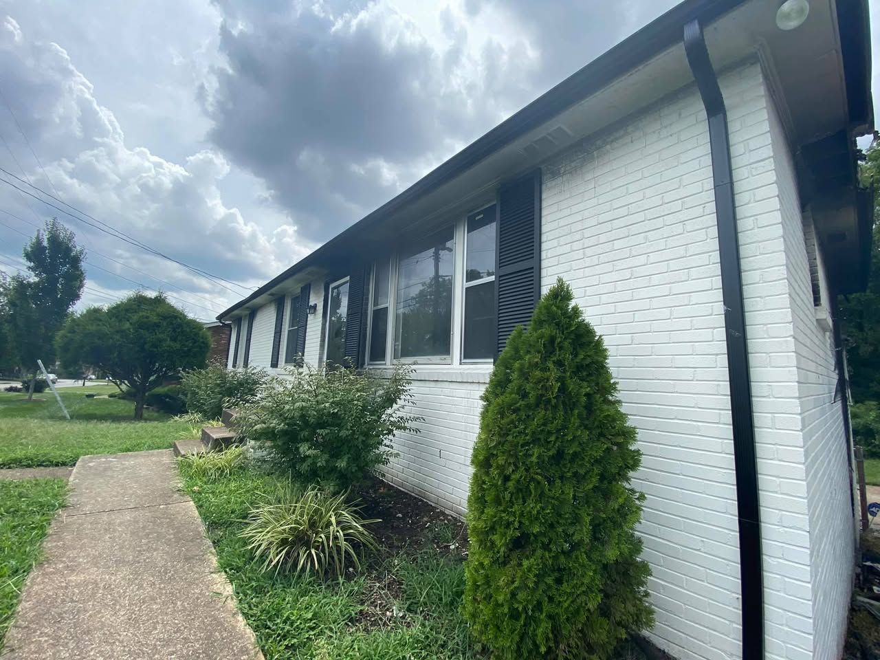 A white brick house with black shutters and a black gutter.