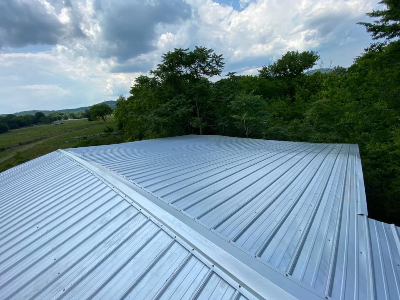 A metal roof with trees in the background and a cloudy sky.