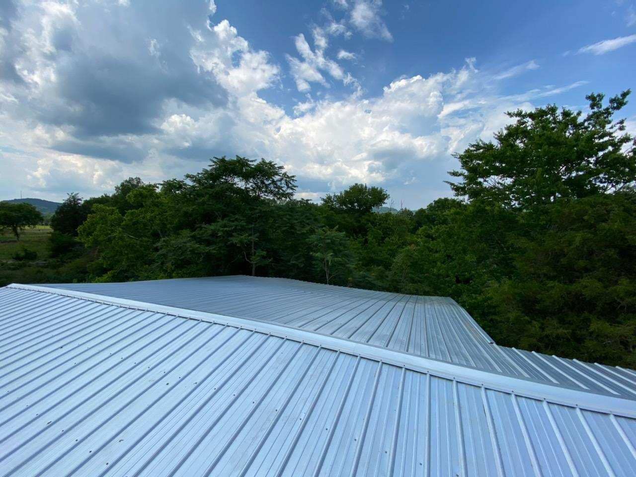 A metal roof with trees in the background and a blue sky with clouds
