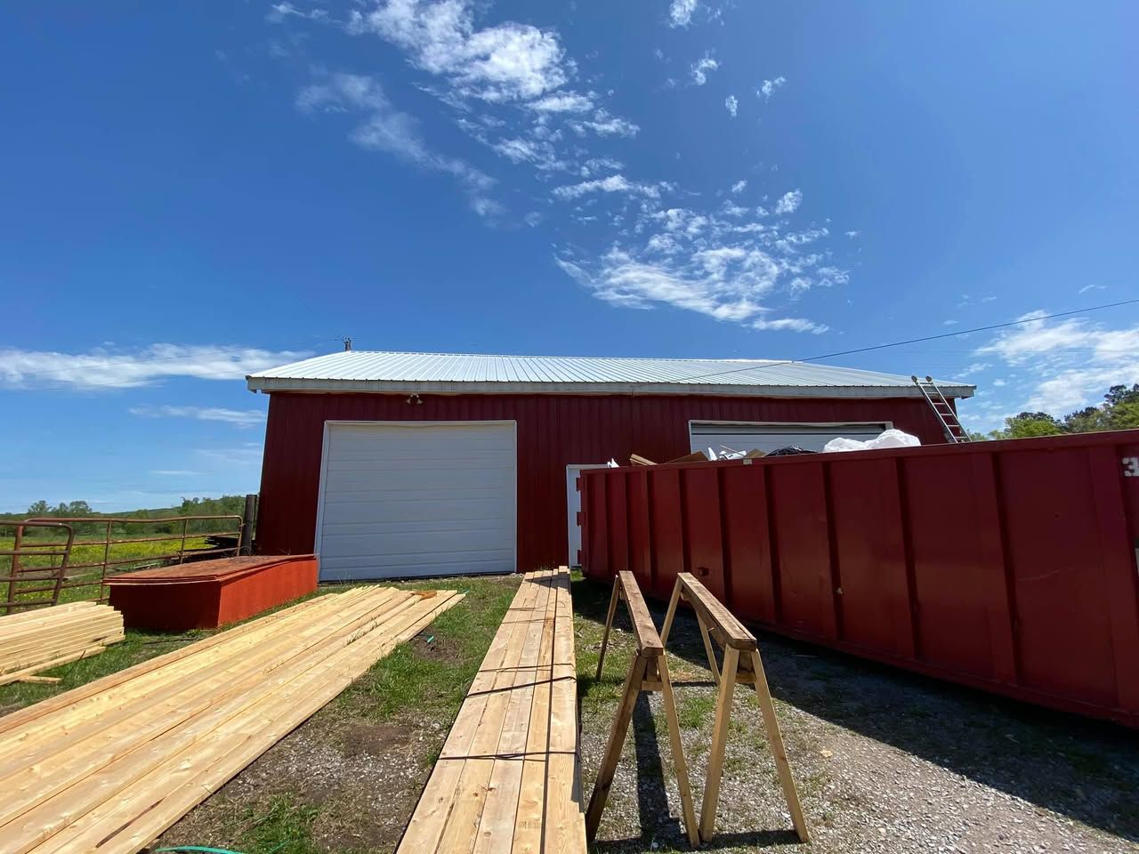 A red barn with a white garage door is being built on a sunny day.