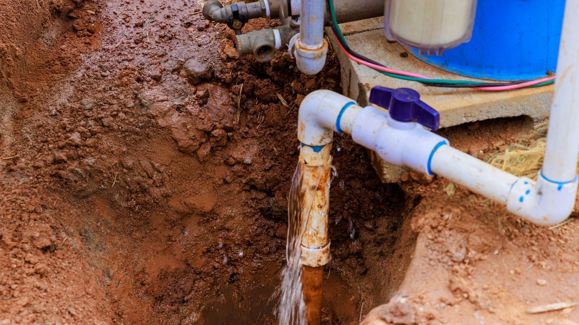 Water gushing from a corroded pipe in a dirt trench.