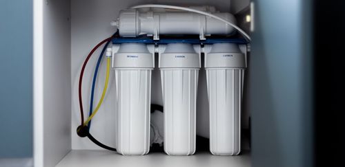 Water filtration system with three white filters inside a white cabinet.