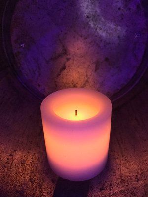 A candle is lit up in a dark room with a purple light behind it.