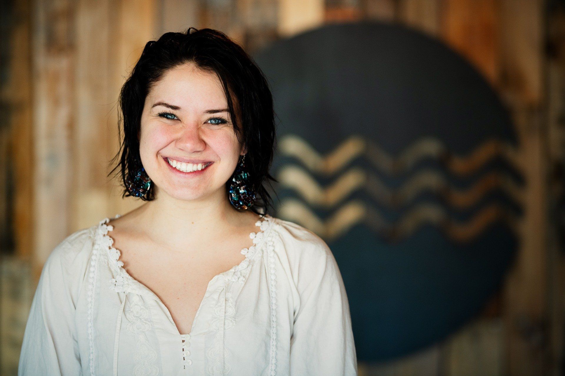 A woman in a white shirt is smiling in front of a wooden wall.