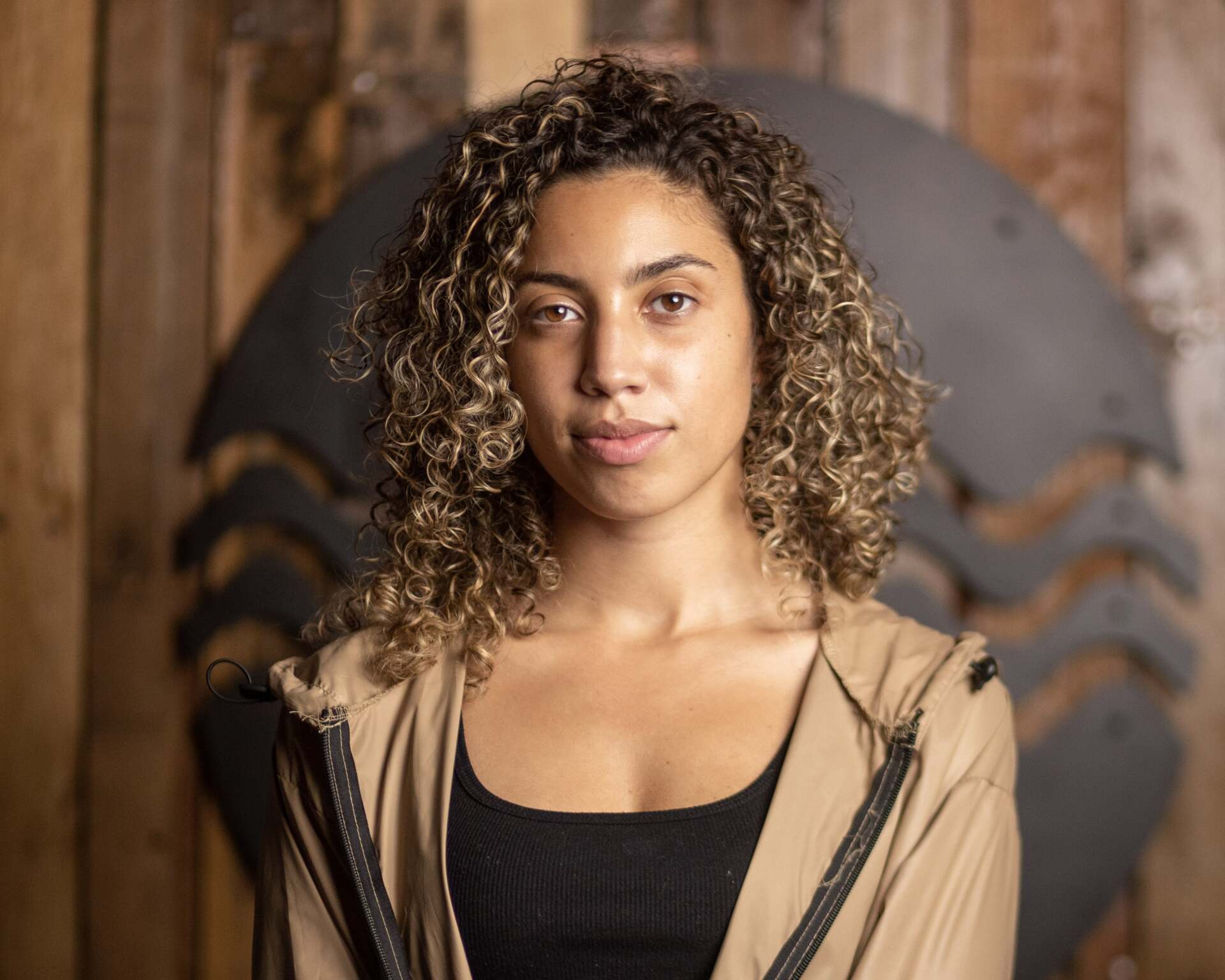 A woman with curly hair is standing in front of a wooden wall.