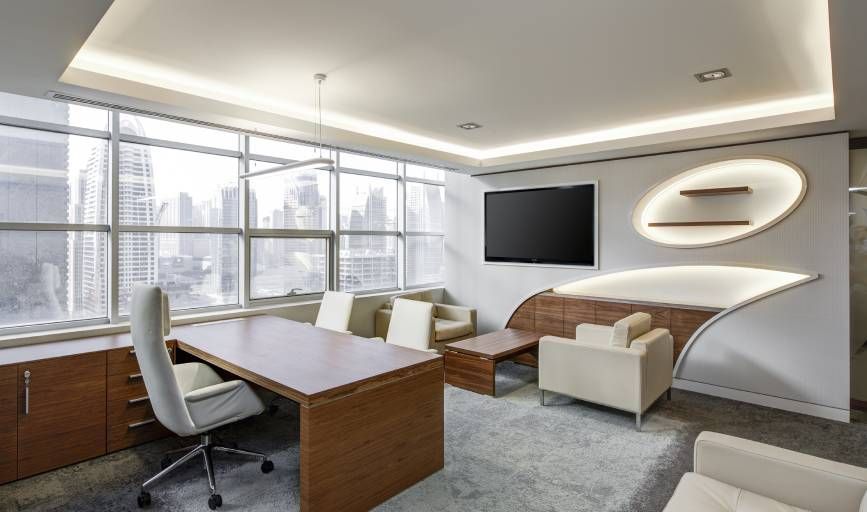 A modern office with a desk , chairs , and a flat screen tv.