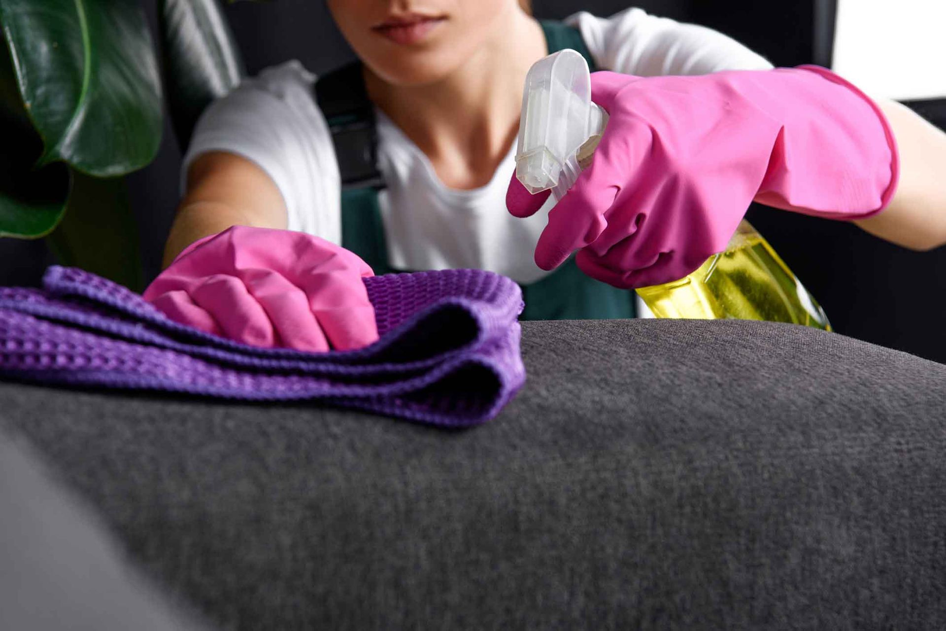 A woman in pink gloves is cleaning a couch with a cloth.