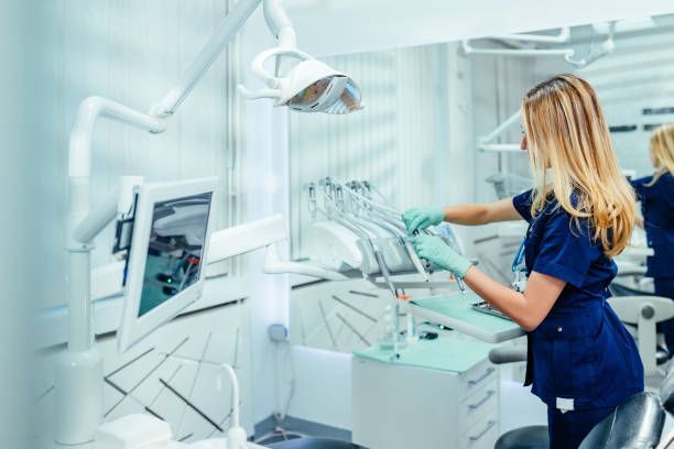 Dentist in blue scrubs cleaning tools in a bright, modern dental office.