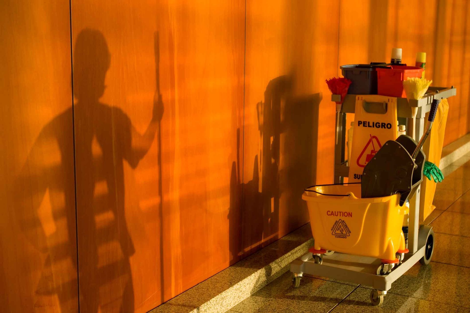 A shadow of a person is cast on a wall next to a cleaning cart.