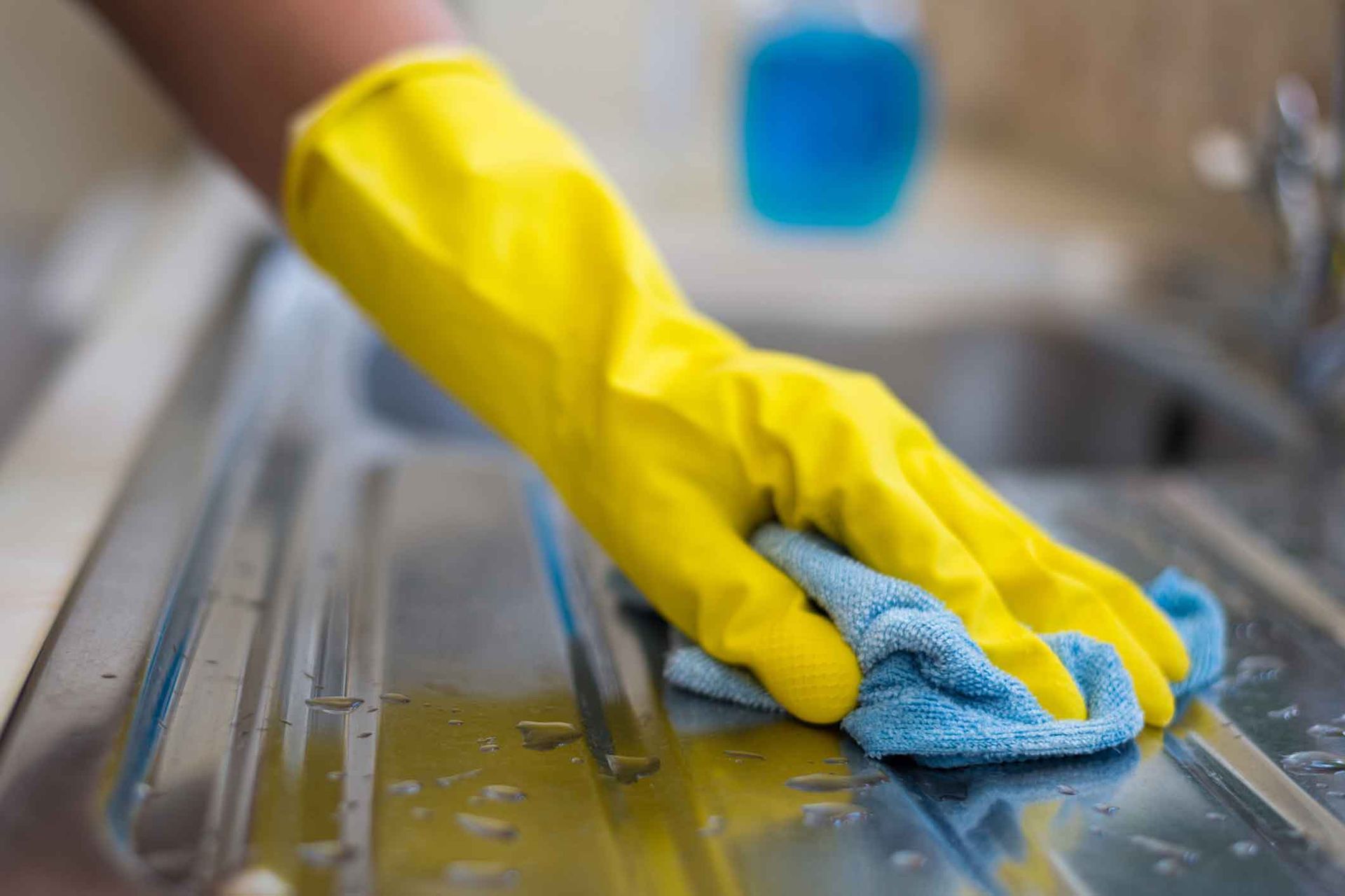 A person wearing yellow gloves is cleaning a sink with a cloth.