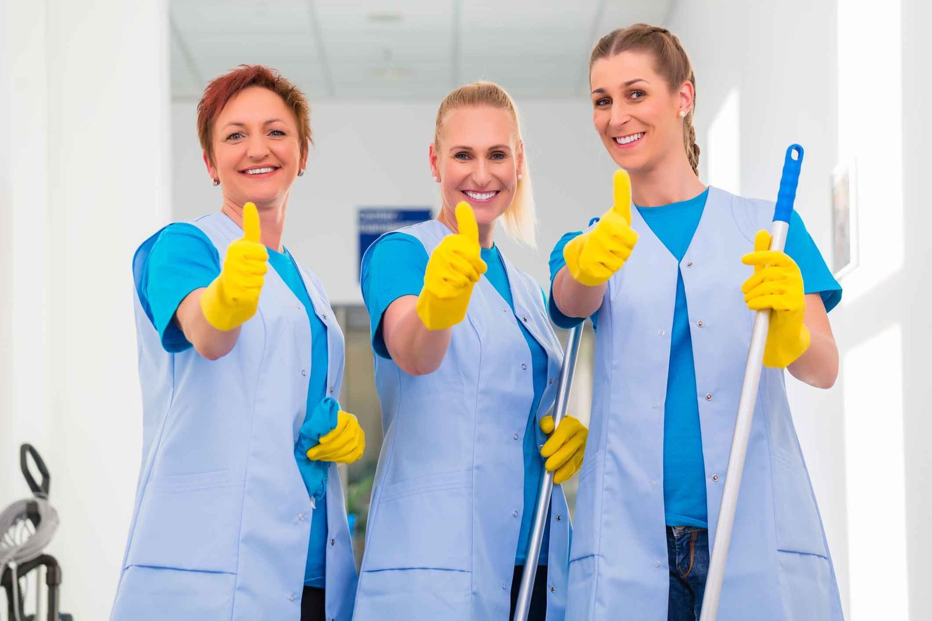 Three female cleaners are giving a thumbs up sign while holding mops.