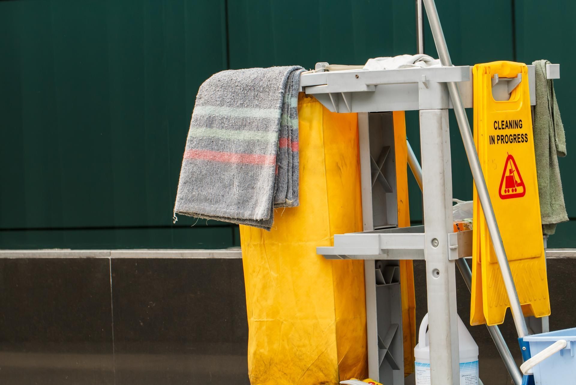 A yellow wet floor sign is hanging on a cleaning cart.