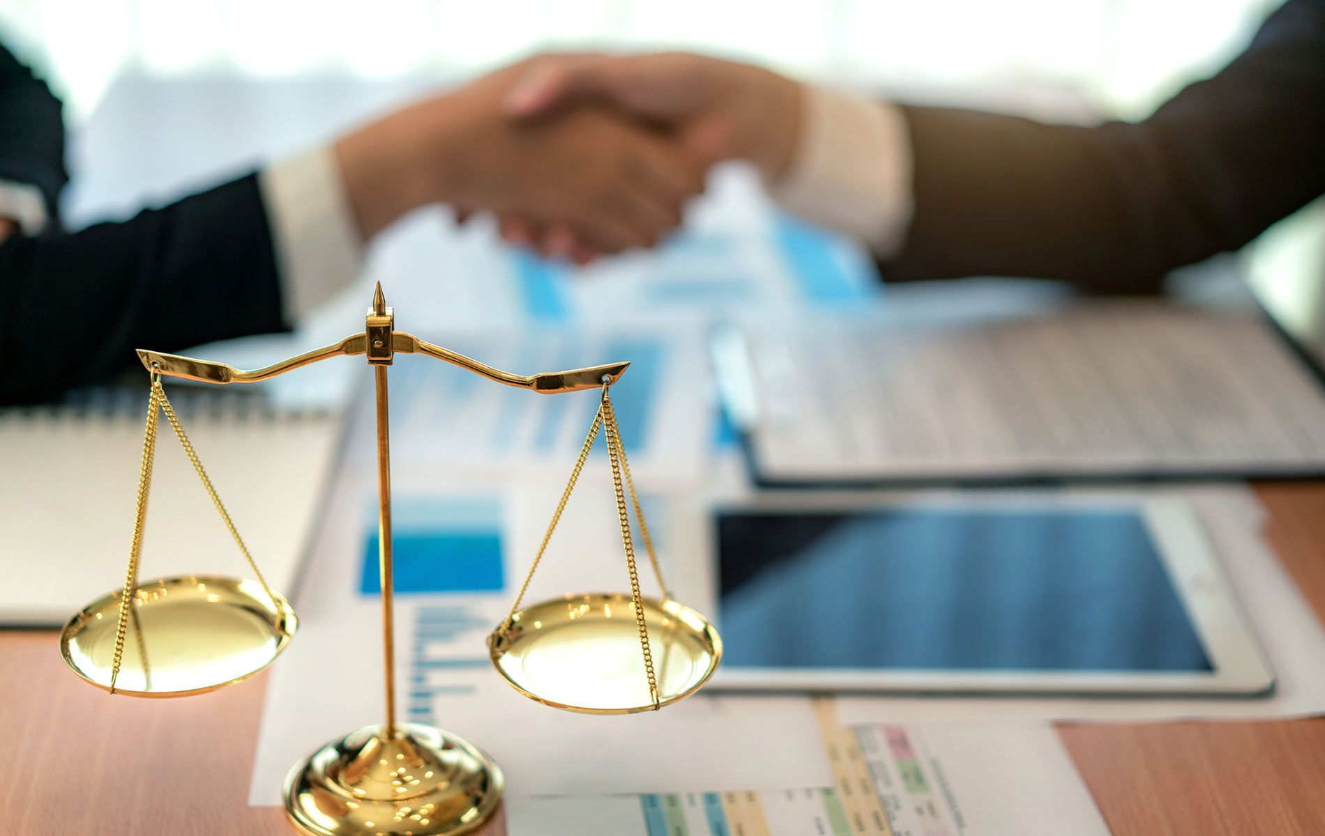 A scale of justice is sitting on a table next to two people shaking hands.