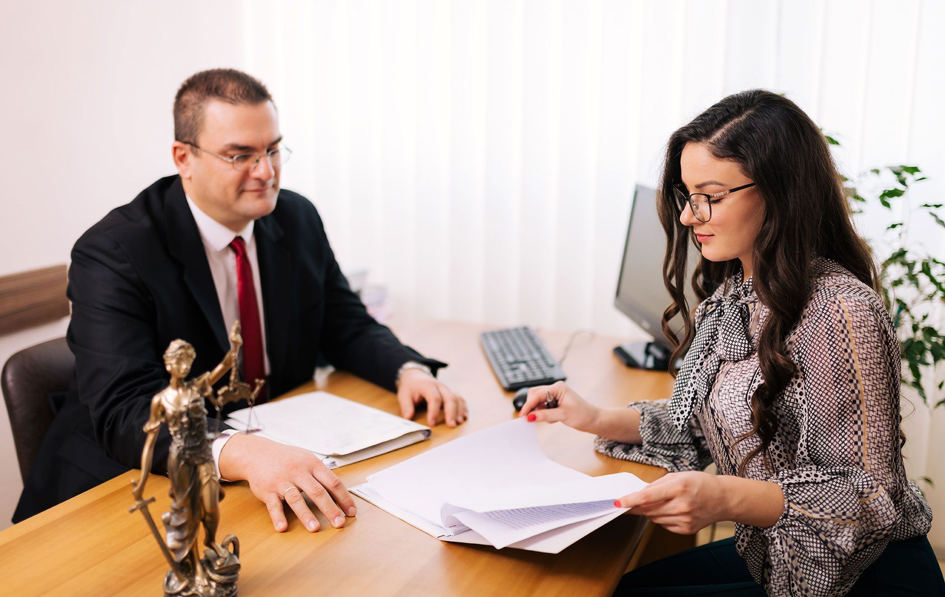 A man and a woman are sitting at a table with a statue of justice.