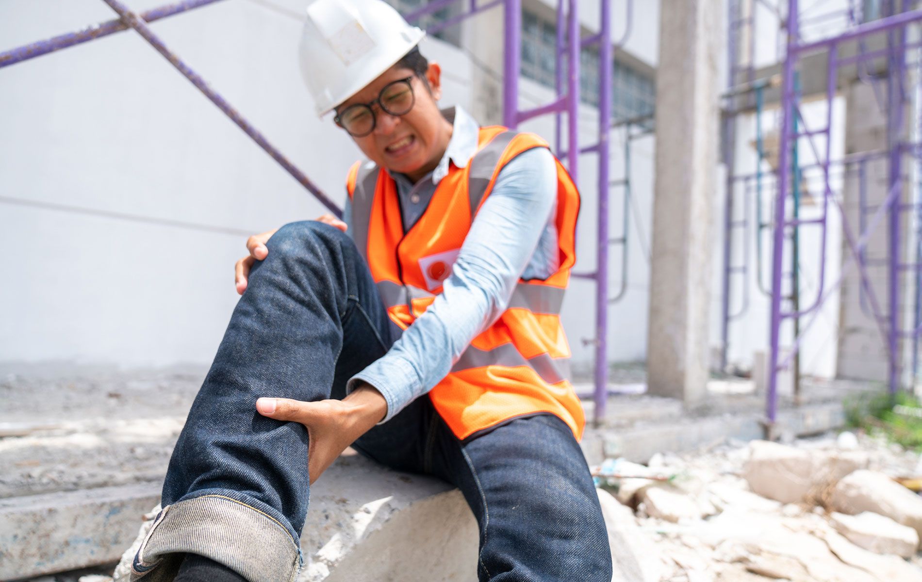 A construction worker is sitting on a concrete block holding his knee.