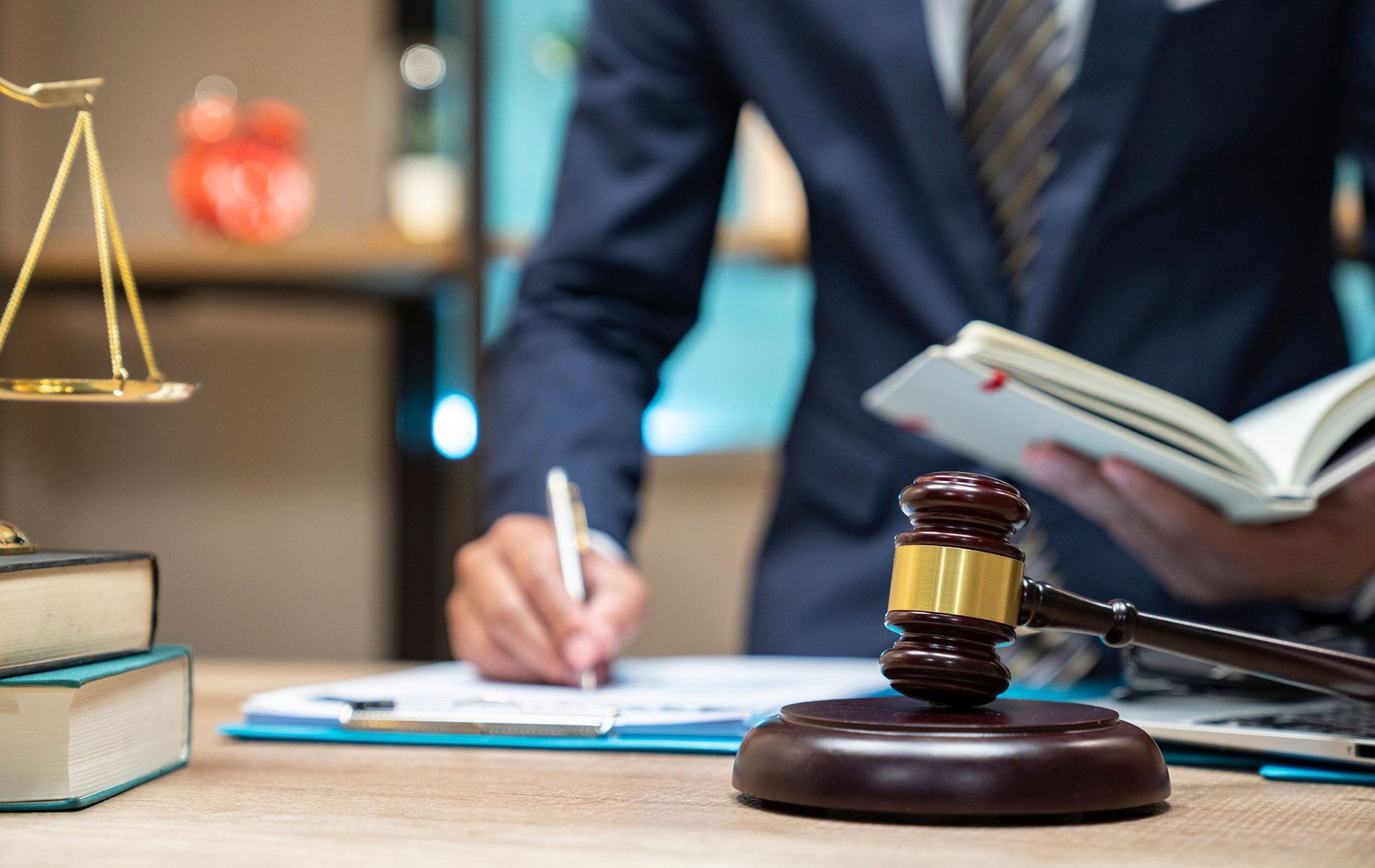 A judge is sitting at a desk holding a book and a gavel.