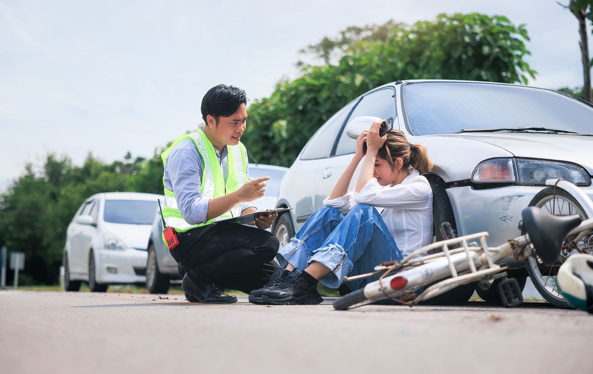 A man is helping a woman who is sitting on the ground after a car and motorcycle accident.
