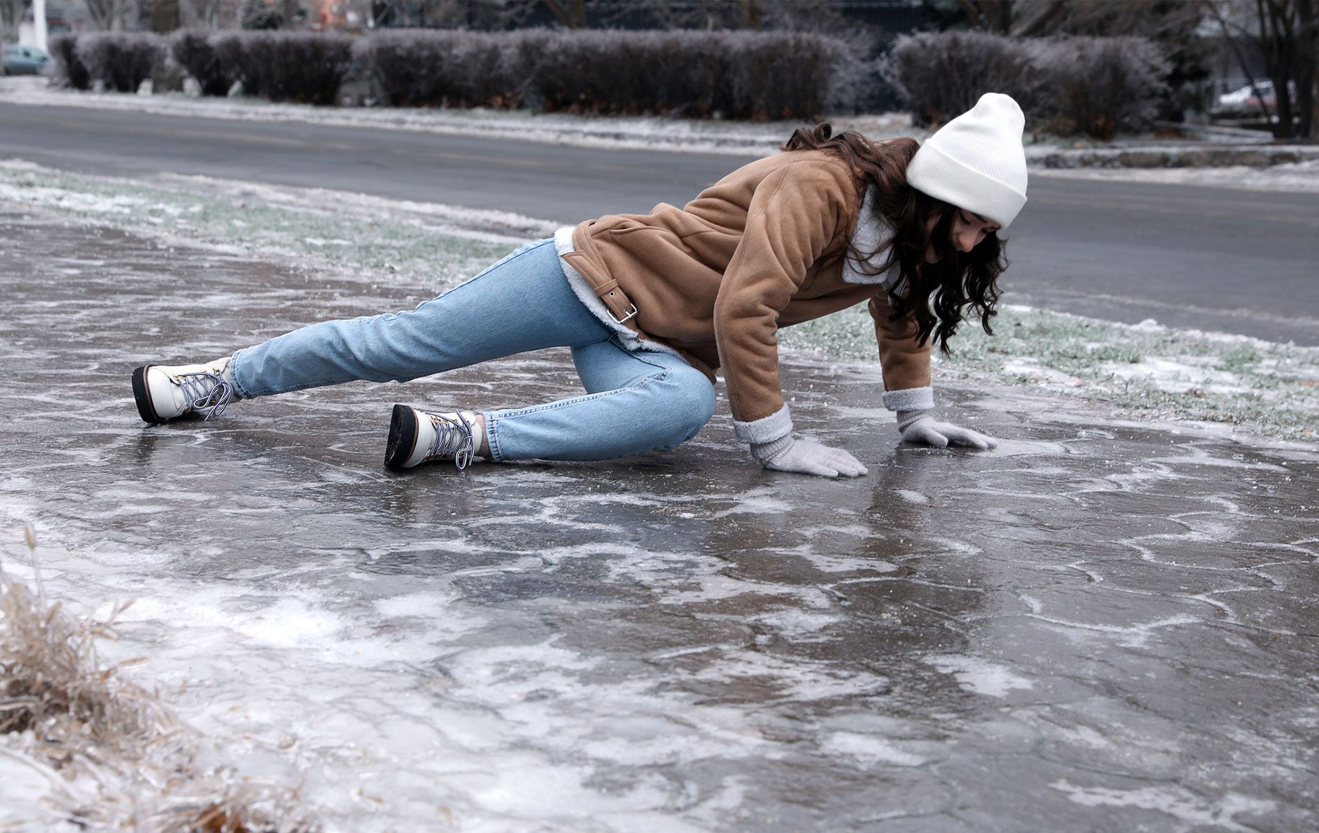 A woman is crawling on the ice on the sidewalk.