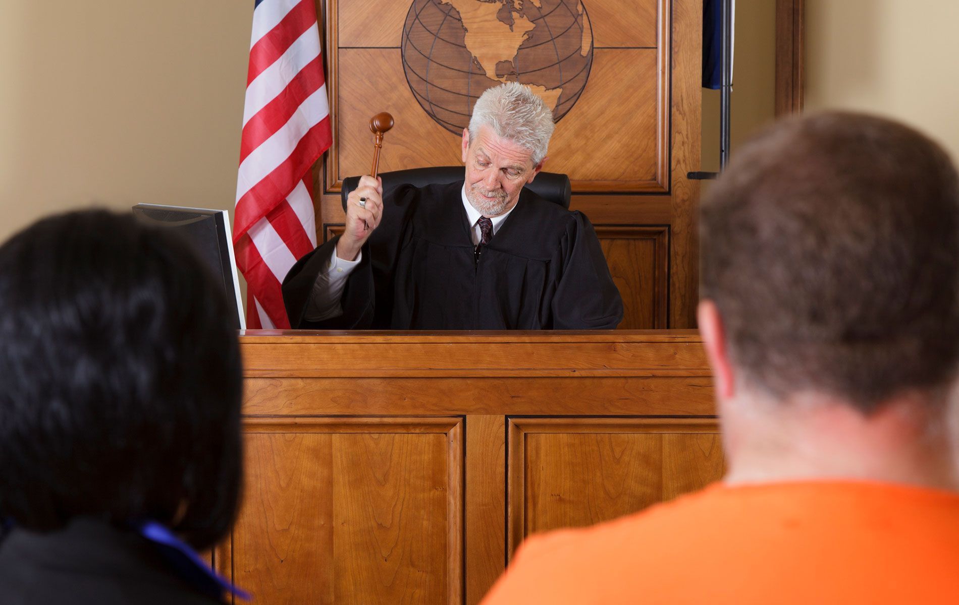 A man in an orange shirt is sitting in front of a judge in a courtroom.